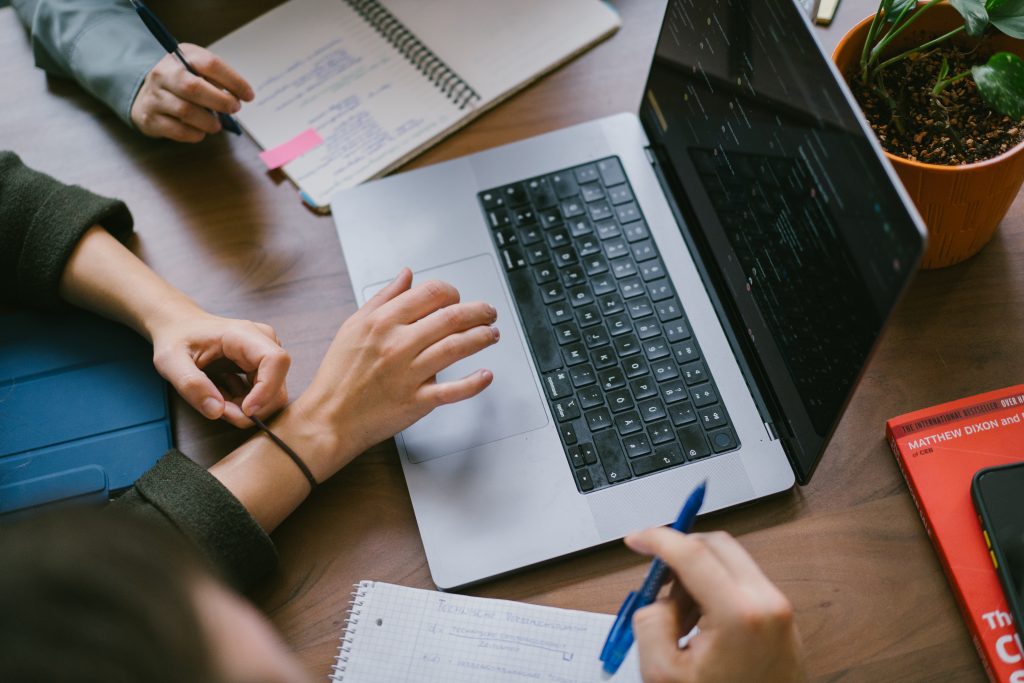 Zwei Personen, die an einem Laptop arbeiten, während sie Notizen machen und einen Stift halten. | Mave Consulting