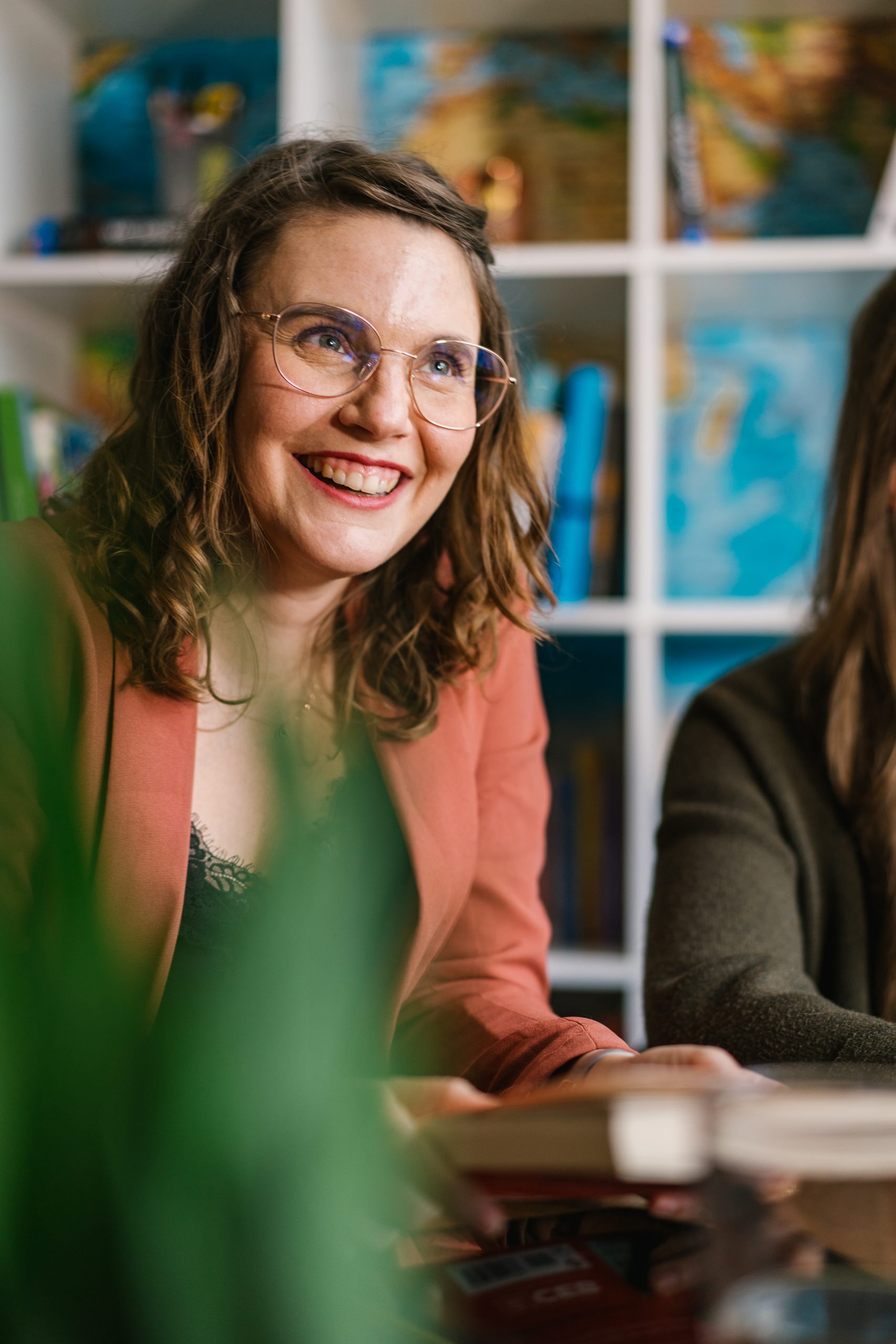 Frau (Sabina Kubik) mit lockigem Haar und Brille, die in einem Meeting lächelt | Mave Consulting