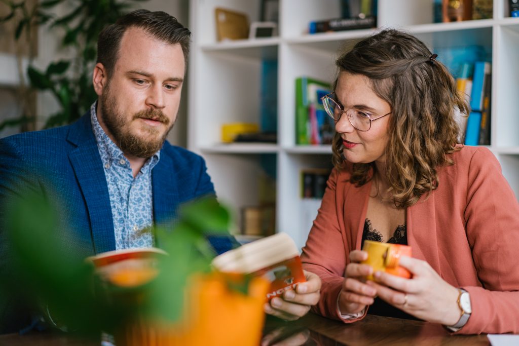 Mann und Frau sitzen an einem Tisch und lesen gemeinsam ein Buch in einem modernen Raum. | Mave Consulting