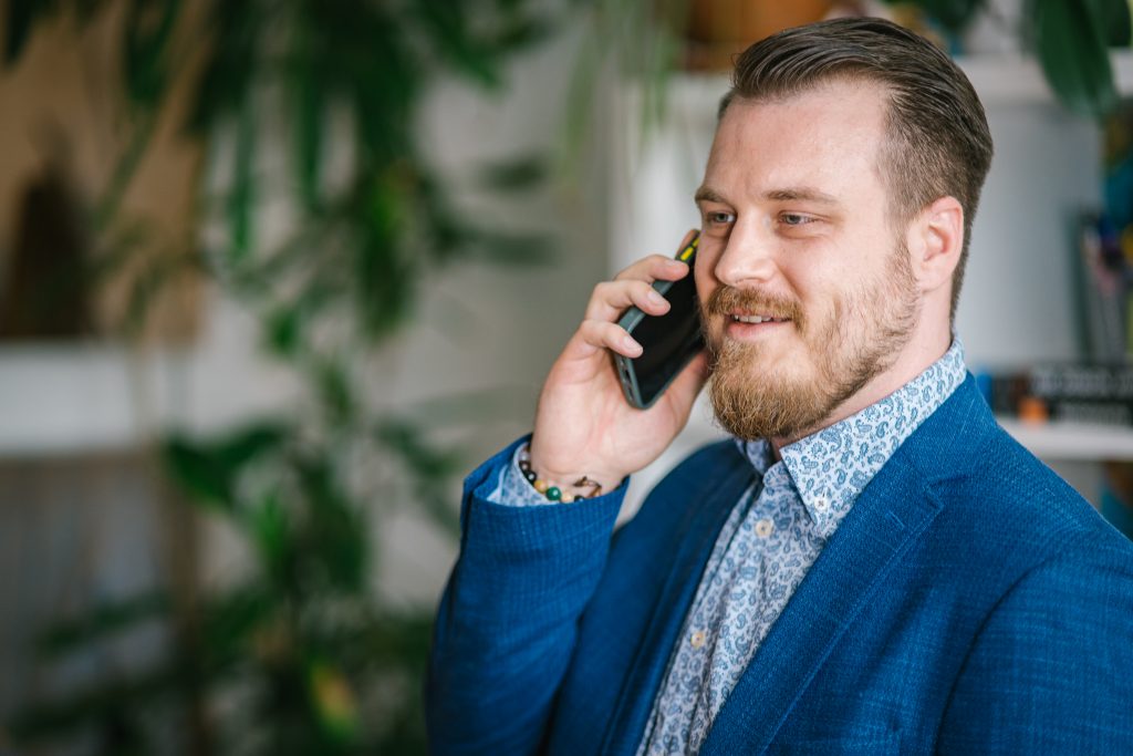 Mann mit Bart und Anzug, der mit einem Smartphone telefoniert, während er lächelt. | Mave Consulting