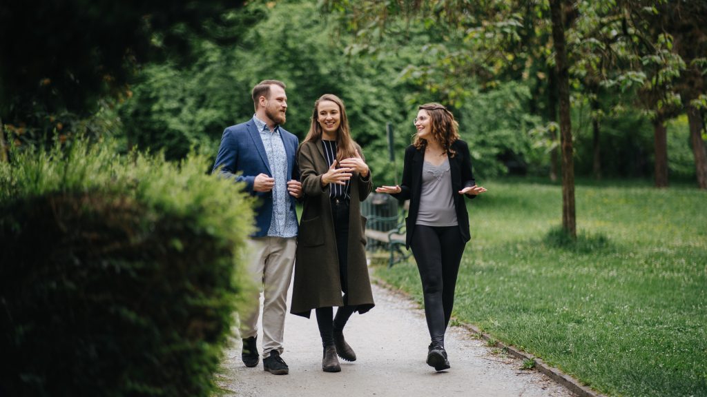 Drei Personen, zwei Frauen und ein Mann, gehen in einem Park und unterhalten sich. | Mave Consulting