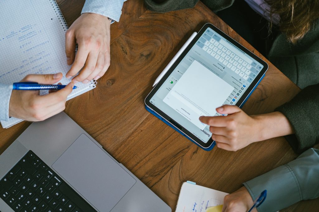 Zwei Hände, die ein Tablet und Notizen auf einem Holztisch verwenden. | Mave Consulting